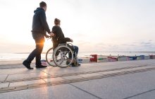 Eine Person im Rollstuhl wird über die Promenade geschoben