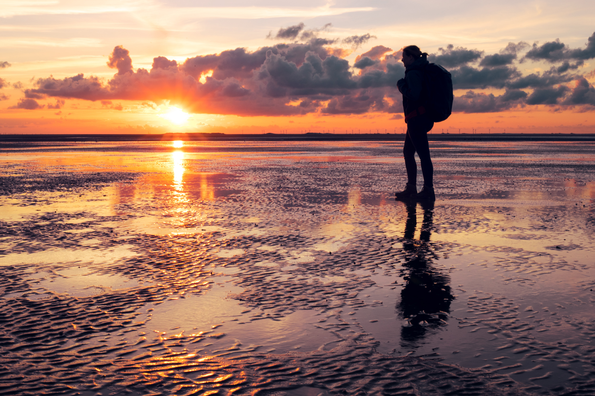 Ein Spaziergänger am Strand vor der untergehenden Sonne